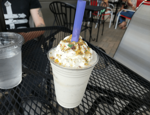 A creamy milkshake topped with whipped cream and colorful sprinkles, served in a clear cup with a blue straw.