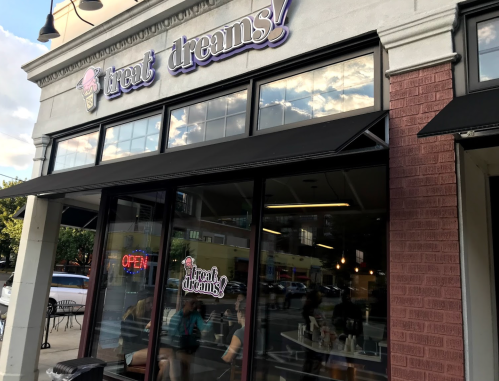 Exterior of "treat dreams!" ice cream shop with an open sign and large windows, showcasing a welcoming atmosphere.