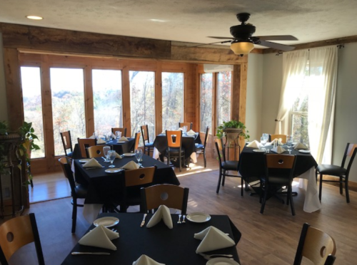 Cozy restaurant interior with wooden accents, tables set for dining, and large windows showcasing a scenic view.