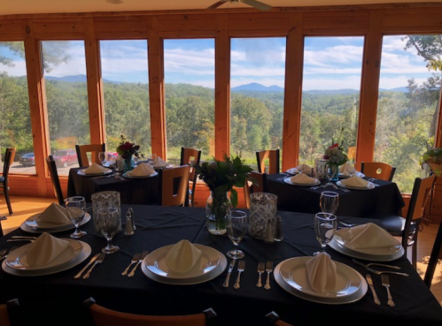 Elegant dining setup with black tablecloths, white napkins, and a scenic view of mountains through large windows.