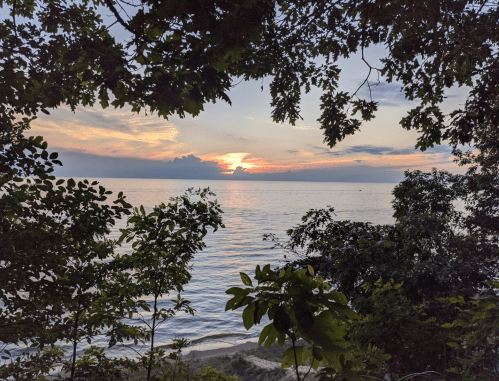 A serene sunset over a calm lake, framed by lush green trees and a colorful sky.