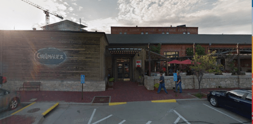 Exterior view of a rustic restaurant with a wooden facade, outdoor seating, and people walking by.