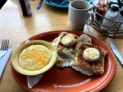 A plate with two pieces of toast topped with egg and a side of cheesy grits, accompanied by a cup of coffee.