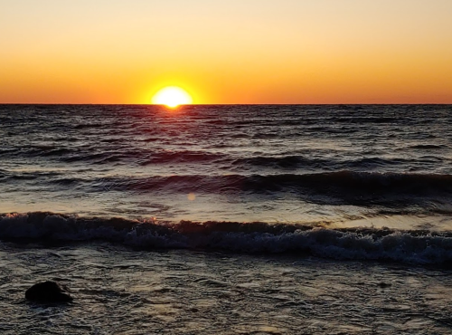 A vibrant sunset over the ocean, with waves gently lapping at the shore and a warm orange sky.