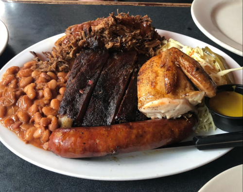 A platter featuring pulled pork, beef ribs, smoked sausage, chicken, baked beans, and coleslaw.