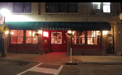 A nighttime view of the Riverfront restaurant, featuring a green awning and warmly lit windows.