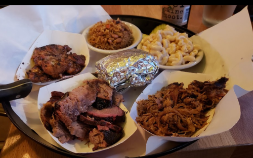 A platter featuring smoked meats, macaroni and cheese, rice, and a foil-wrapped baked potato.