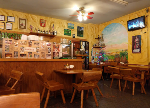 Cozy restaurant interior with wooden tables, a colorful mural, and a small Christmas tree, featuring a warm ambiance.