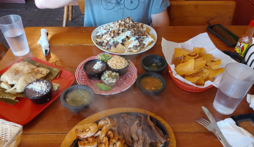 A table with a variety of dishes: nachos, grilled shrimp, steak, tortillas, rice, and chips with sauces.
