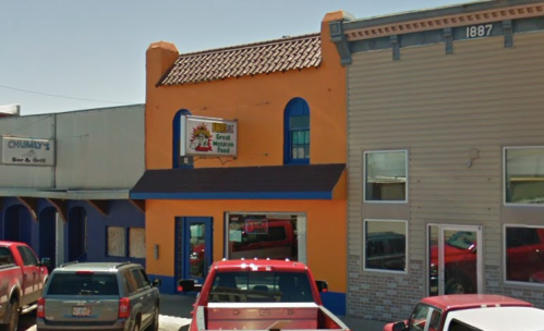 A colorful orange building with a sign for "Great Mexican Food" next to a bar and grill, parked cars in front.