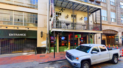 A white pickup truck parked in front of a building with a balcony and an entrance sign, in an urban setting.