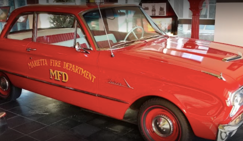 A vintage red car with "Marietta Fire Department" and "MFD" lettering displayed in a museum setting.