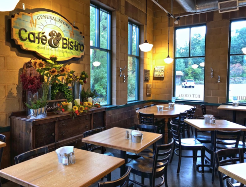 Cozy café interior with wooden tables, large windows, and a vibrant flower display near the entrance.