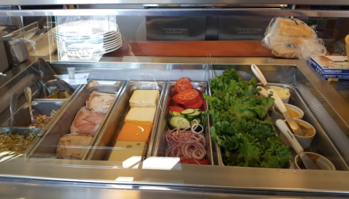 A deli counter with various sandwich ingredients: meats, cheeses, vegetables, and condiments in metal trays.