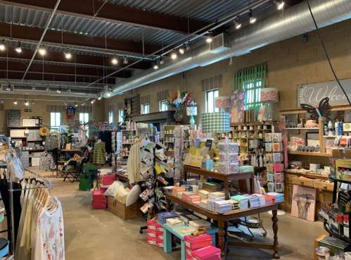 A vibrant store interior filled with colorful merchandise, including cards, gifts, and clothing, under bright lighting.