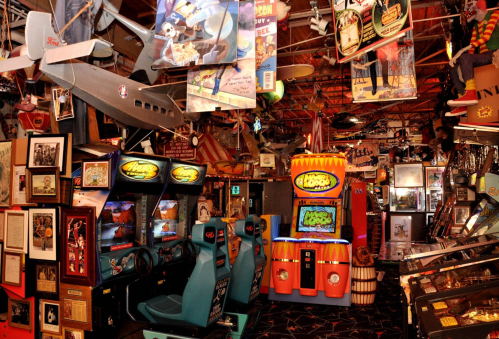 A vibrant arcade filled with vintage games, colorful decor, and hanging memorabilia from various eras.