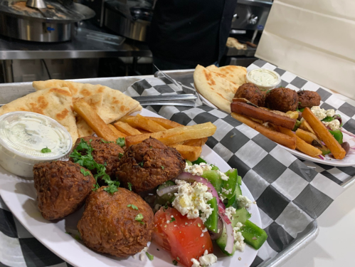 Two plates of food featuring falafel balls, fries, pita bread, and a fresh salad with tomatoes and feta cheese.