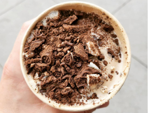 A close-up of a dessert cup topped with crushed chocolate and cookie pieces, held in a hand.