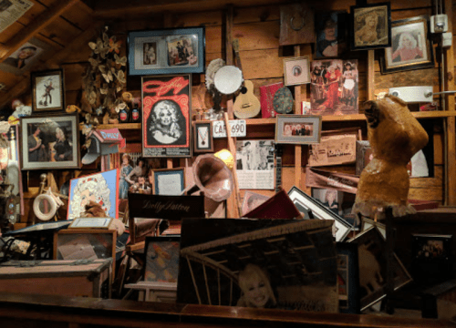 A cluttered wall filled with various framed photos, artwork, and memorabilia in a cozy, rustic setting.