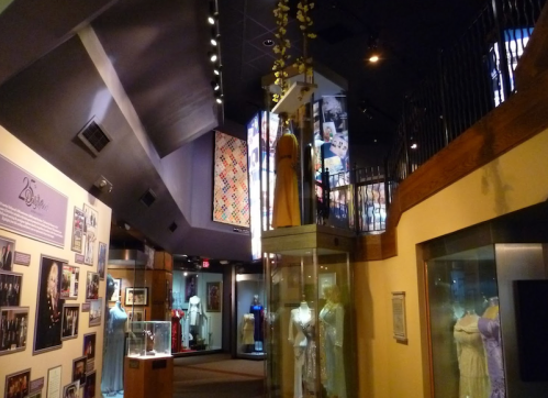 Interior of a museum showcasing elegant dresses, with displays and photographs on the walls.