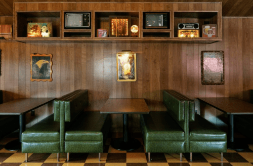 Retro diner interior with green booths, wooden paneling, and vintage decor, including old TVs on a shelf.