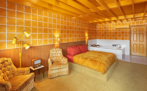 A retro-style bedroom with orange patterned walls, a large fur bedspread, and vintage furniture.