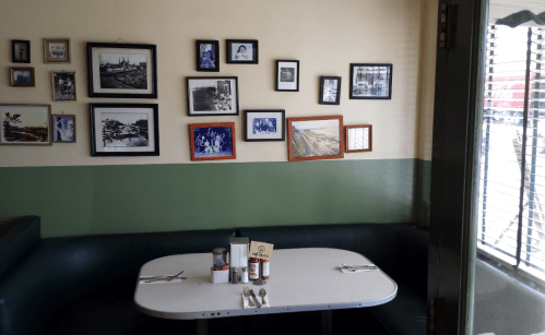 A cozy diner booth with a white table, silverware, and a wall adorned with framed black-and-white photos.
