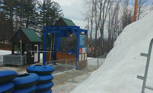 A snow-covered area with a tubing lift station and blue inner tubes stacked nearby, surrounded by trees.