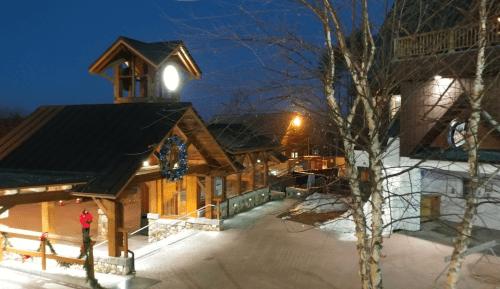 A cozy mountain lodge at dusk, adorned with holiday decorations and soft lights, surrounded by snow.