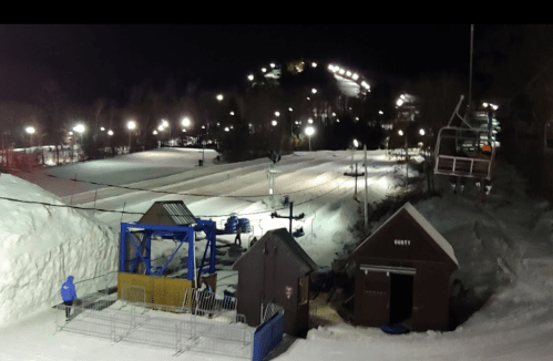 Nighttime view of a ski resort with snow-covered slopes, a chairlift, and illuminated pathways.