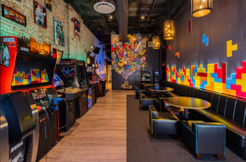 A vibrant arcade with retro game machines, colorful wall art, and cozy seating areas.