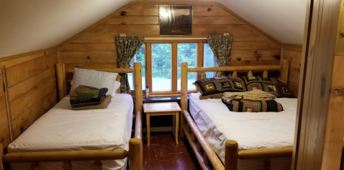 Cozy attic bedroom with two wooden beds, a window, and rustic decor.