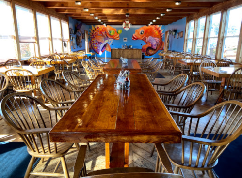 A spacious restaurant interior with wooden tables and chairs, featuring colorful fish murals on the wall.