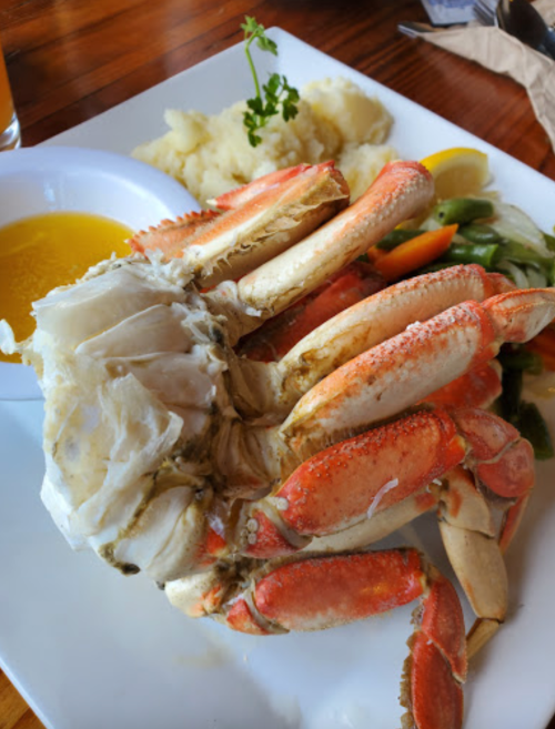 A plate featuring a large crab claw, mashed potatoes, and mixed vegetables with a side of dipping sauce.
