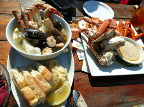 A seafood feast featuring crab, shrimp, mussels, and sides of bread and sweet potato fries on a wooden table.