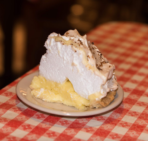 A slice of lemon meringue pie on a white plate, featuring a fluffy meringue topping and a creamy lemon filling.