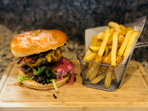 A juicy burger with cheese, lettuce, and onions, served with a side of golden fries in a small metal basket.