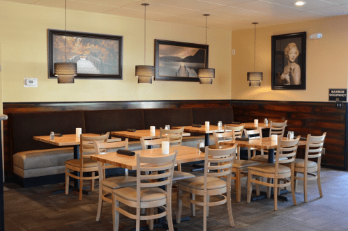 A cozy restaurant interior with wooden tables, chairs, and framed artwork on the walls. Soft lighting creates a warm atmosphere.