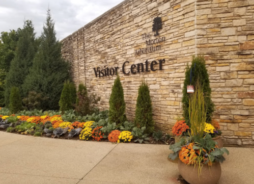 Stone wall with "Visitor Center" sign, surrounded by colorful flowers and greenery at The Morton Arboretum.