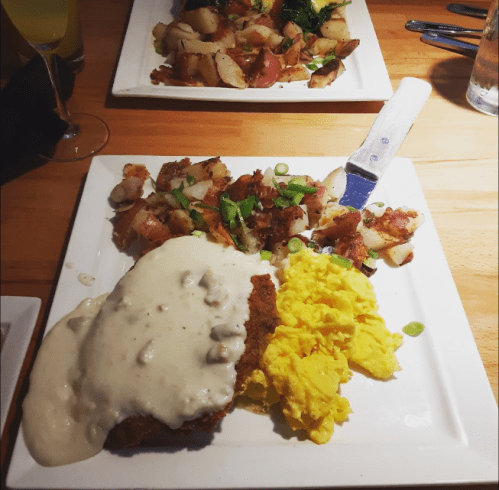 A plate of chicken fried steak with gravy, scrambled eggs, and seasoned potatoes on a wooden table.