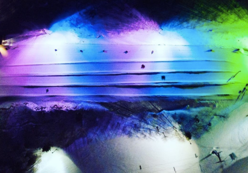 Abstract aerial view of colorful lights reflecting on a textured surface, creating a vibrant, wavy pattern.