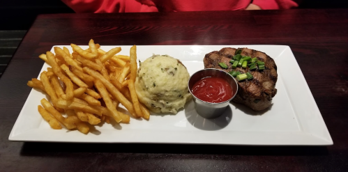 A plate with steak, mashed potatoes, and French fries, served with a small cup of ketchup.