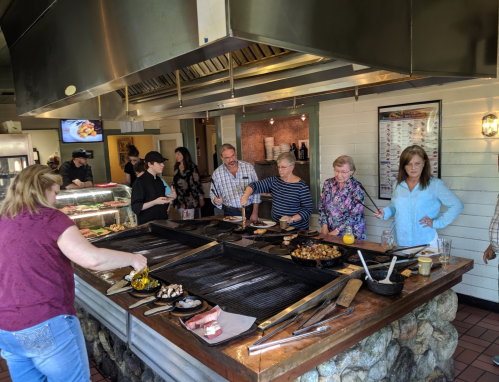 A group of people cooking and serving food at a grill station in a restaurant, with various dishes on display.