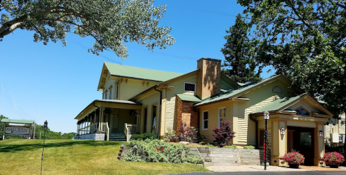 A charming yellow house with a green roof, surrounded by trees and flowers, on a sunny day.