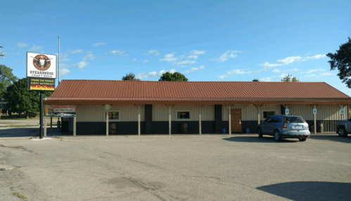A single-story steakhouse with a brown metal roof and parking lot, under a clear blue sky.