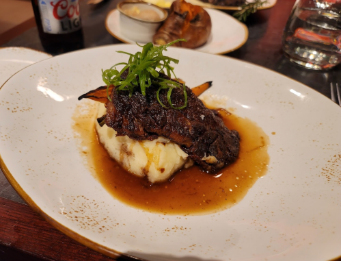 A plate featuring a piece of grilled meat on creamy mashed potatoes, garnished with green onions and a rich sauce.