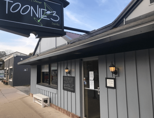 Exterior of Toonie's restaurant, featuring a sign, door with menus, and a gray wooden facade.