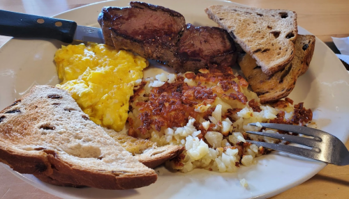 A plate of breakfast featuring steak, scrambled eggs, hash browns, and toasted bread.