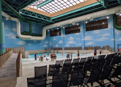 Indoor water park scene with a wave pool, people enjoying the water, and empty seating in the foreground.