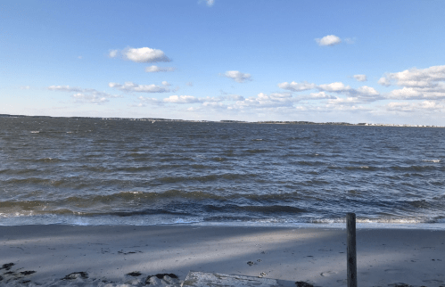 A serene beach scene with gentle waves, sandy shore, and a clear blue sky dotted with clouds.